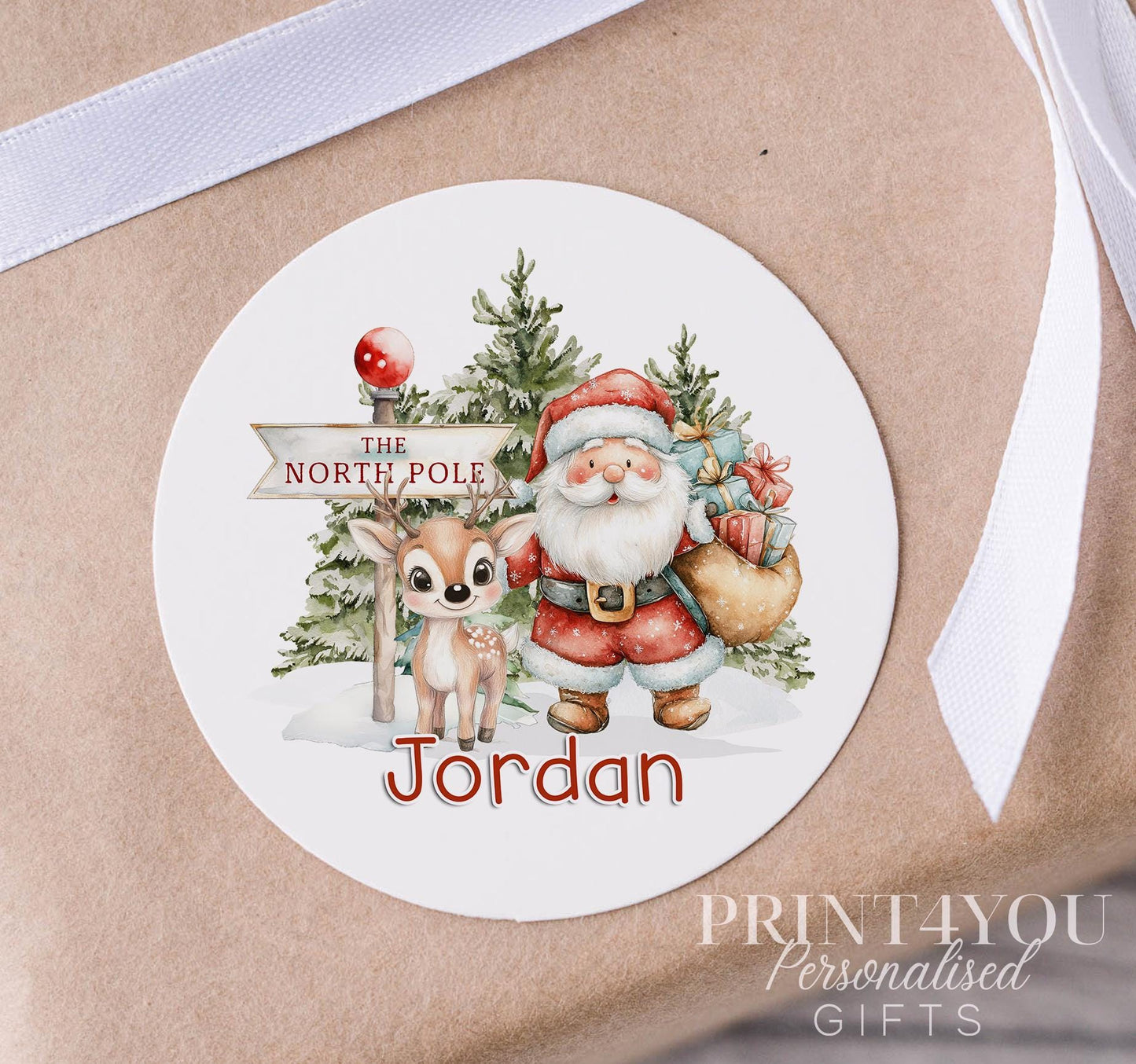Personalised glossy white 5cm Christmas sticker featuring Santa and his reindeer, custom name printed, shown on a strip of stickers