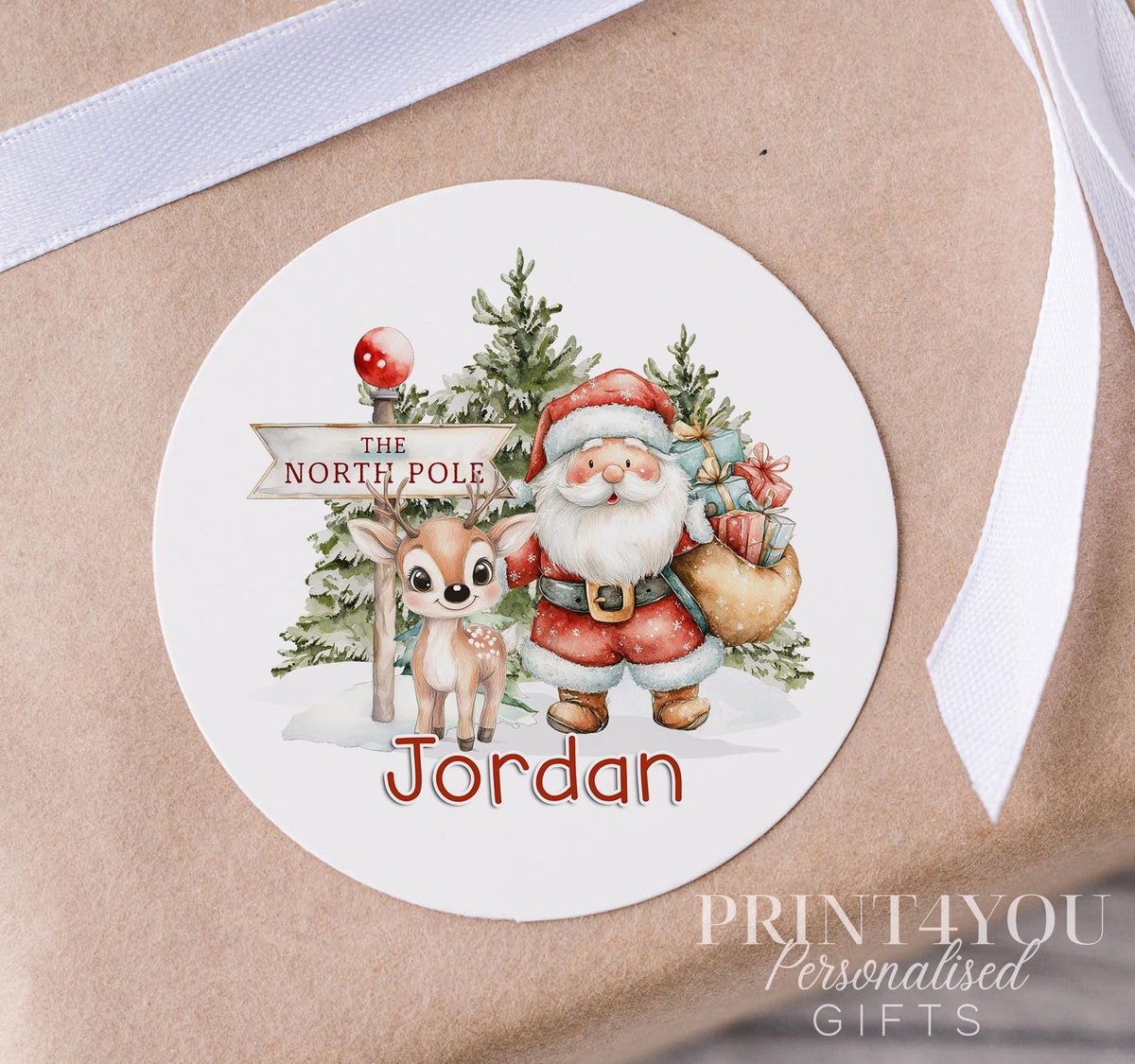 Personalised glossy white 5cm Christmas sticker featuring Santa and his reindeer, custom name printed, shown on a strip of stickers