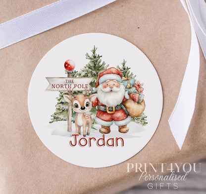 Personalised glossy white 5cm Christmas sticker featuring Santa and his reindeer, custom name printed, shown on a strip of stickers