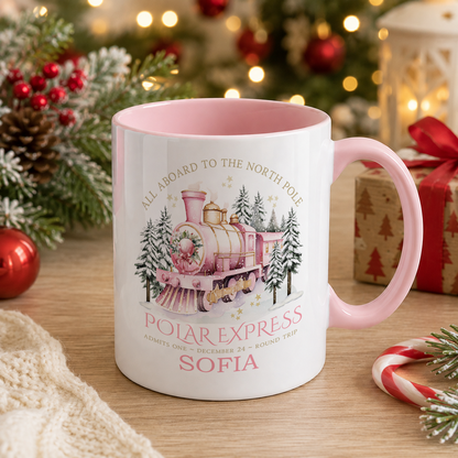 A white mug with a pink interior, featuring an illustration of a pink and white train on a snowy landscape, surrounded by Christmas decorations and gifts.