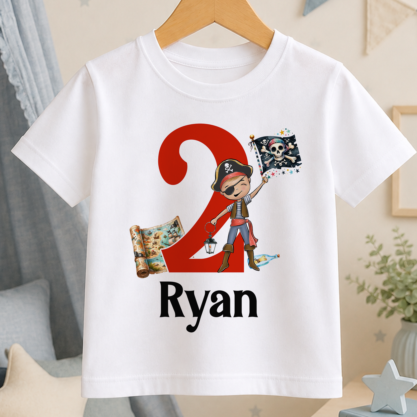 A white t-shirt with a pirate-themed design, including a red number 2, a pirate flag, and a map. The text "Ryan" is printed below the design.
