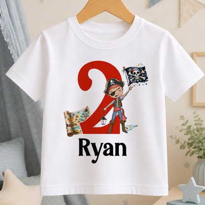 A white t-shirt with a pirate-themed design, including a red number 2, a pirate flag, and a map. The text "Ryan" is printed below the design.
