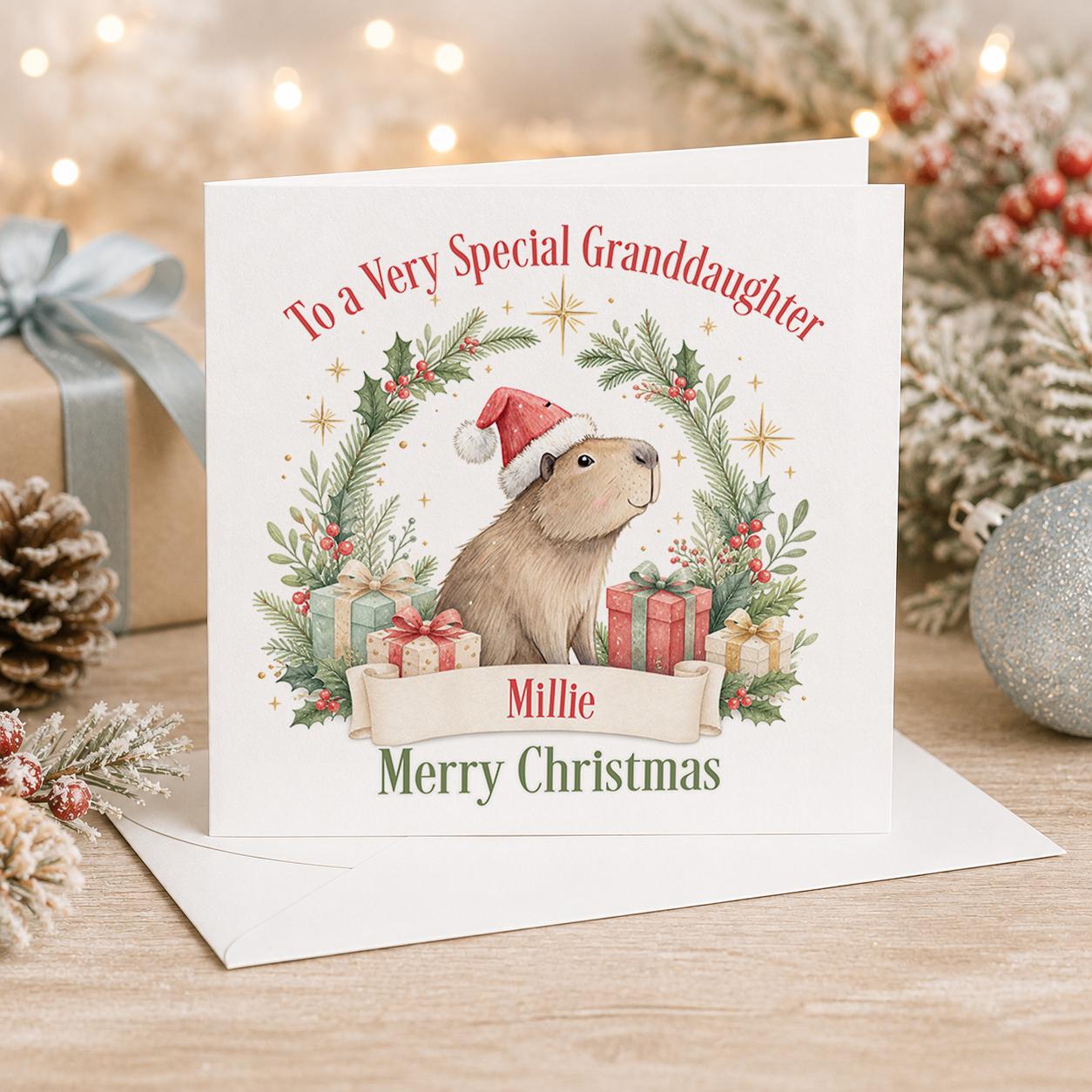 Personalised capybara Christmas card, white 6x6 inch square card printed with a capybara in a Santa hat inside a wreath with a name
