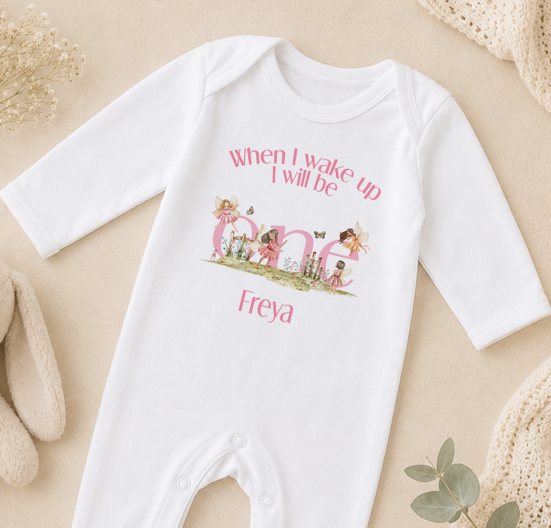White baby onesie personalised with a name and fairy illustrations, laid on a beige surface