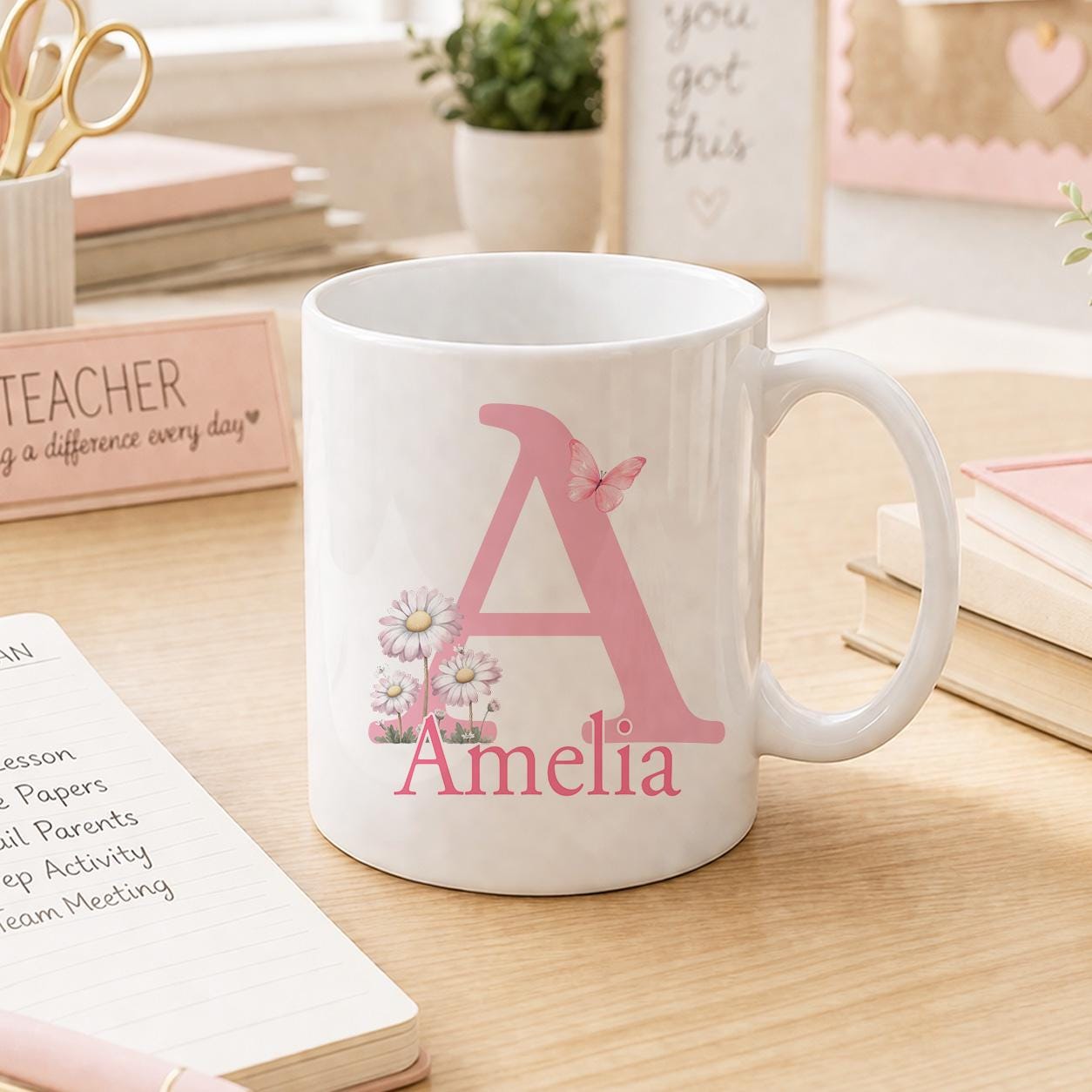 Personalised pink floral initial mug shown from a second angle on a desk with a notebook