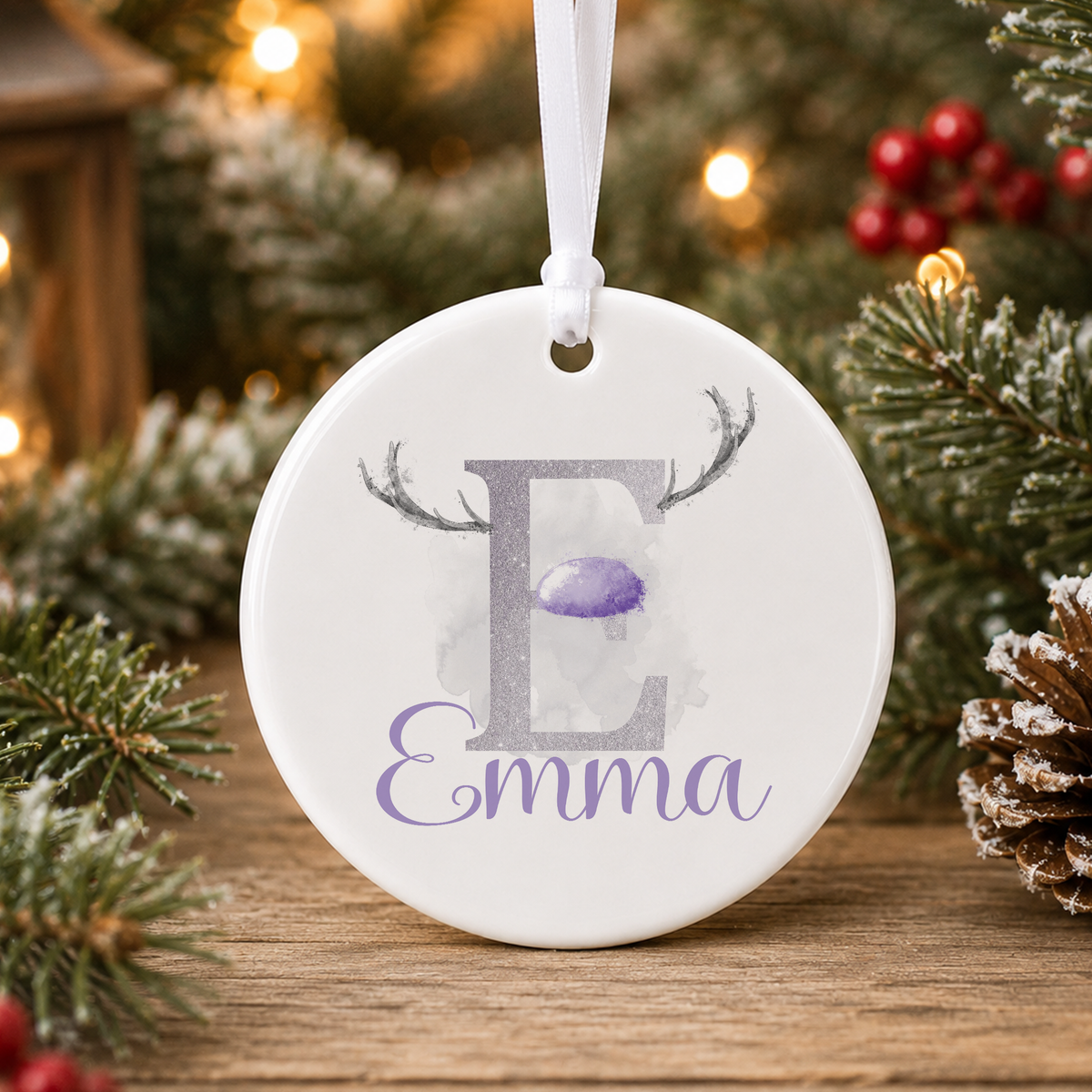 A white oval ornament with the letter "E" and the name "Emma" printed on it, hanging on a Christmas tree.