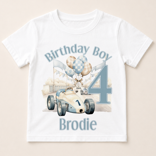 A white t-shirt with a graphic design featuring a race car and balloons, along with the text "Birthday Boy Brodie" and the number "4".
