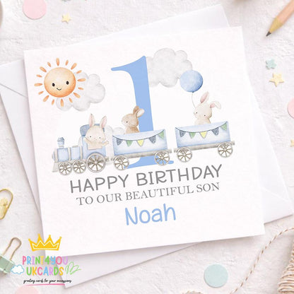 Square personalised first birthday card featuring a blue train and bunny design on a plain background