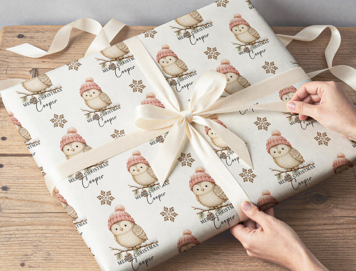 Two gifts wrapped in owl and snowflake Christmas paper tied with cream ribbon on a wooden table.