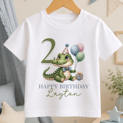 White cotton kids T-shirt printed with a cartoon crocodile wearing a party hat and holding balloons, personalised with a birthday name and age.