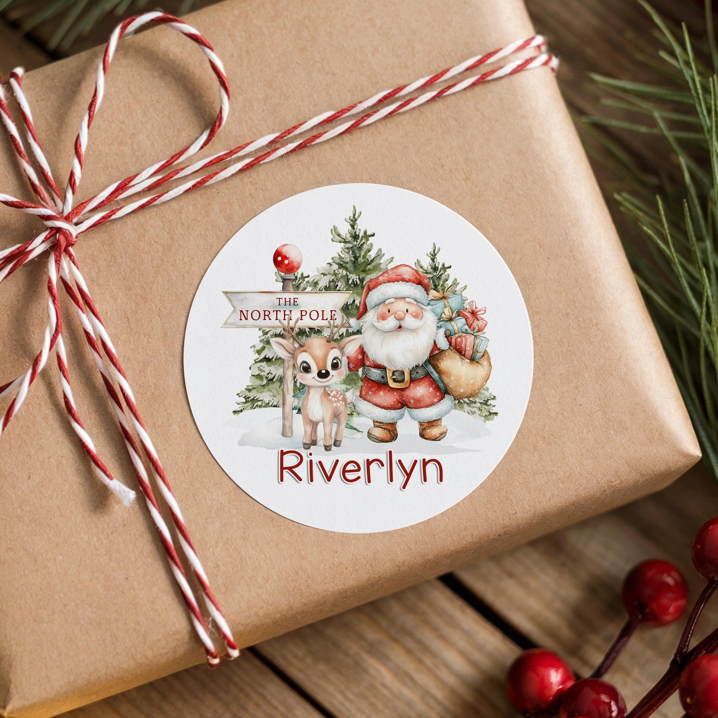Personalised Santa and reindeer Christmas sticker with a snowy North Pole scene, stuck on a gift box wrapped with twine, printed with a custom name
