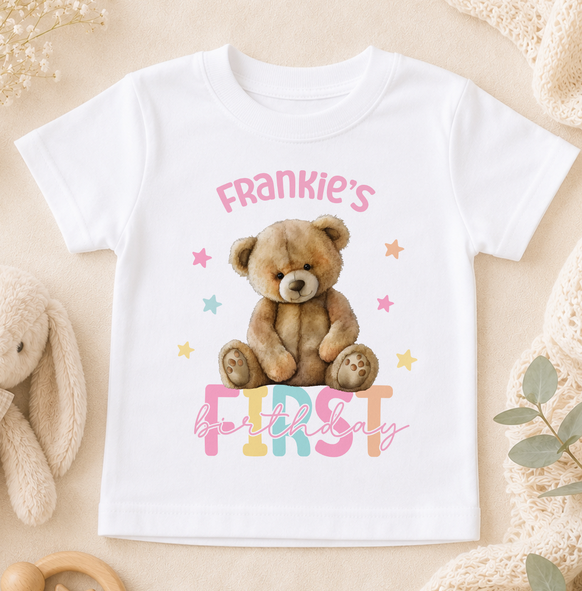 A white t-shirt with a teddy bear and the text "Frankie's first birthday" printed on it.