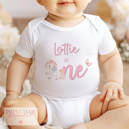 Personalised pastel unicorn bib for a baby's first birthday, printed with a custom name and rainbow butterfly design.