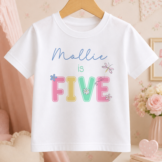 A white t-shirt with the text "Mollie is FIVE" printed on it, along with colorful flower designs.