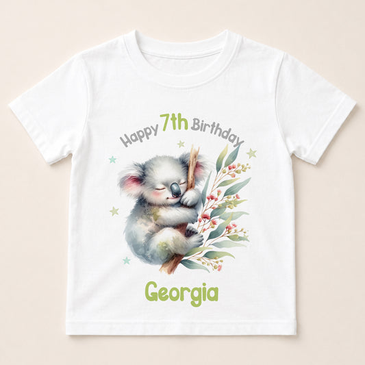 A white t-shirt with a printed design featuring a koala bear and some greenery. The text on the t-shirt reads "Happy 7th Birthday Georgia".