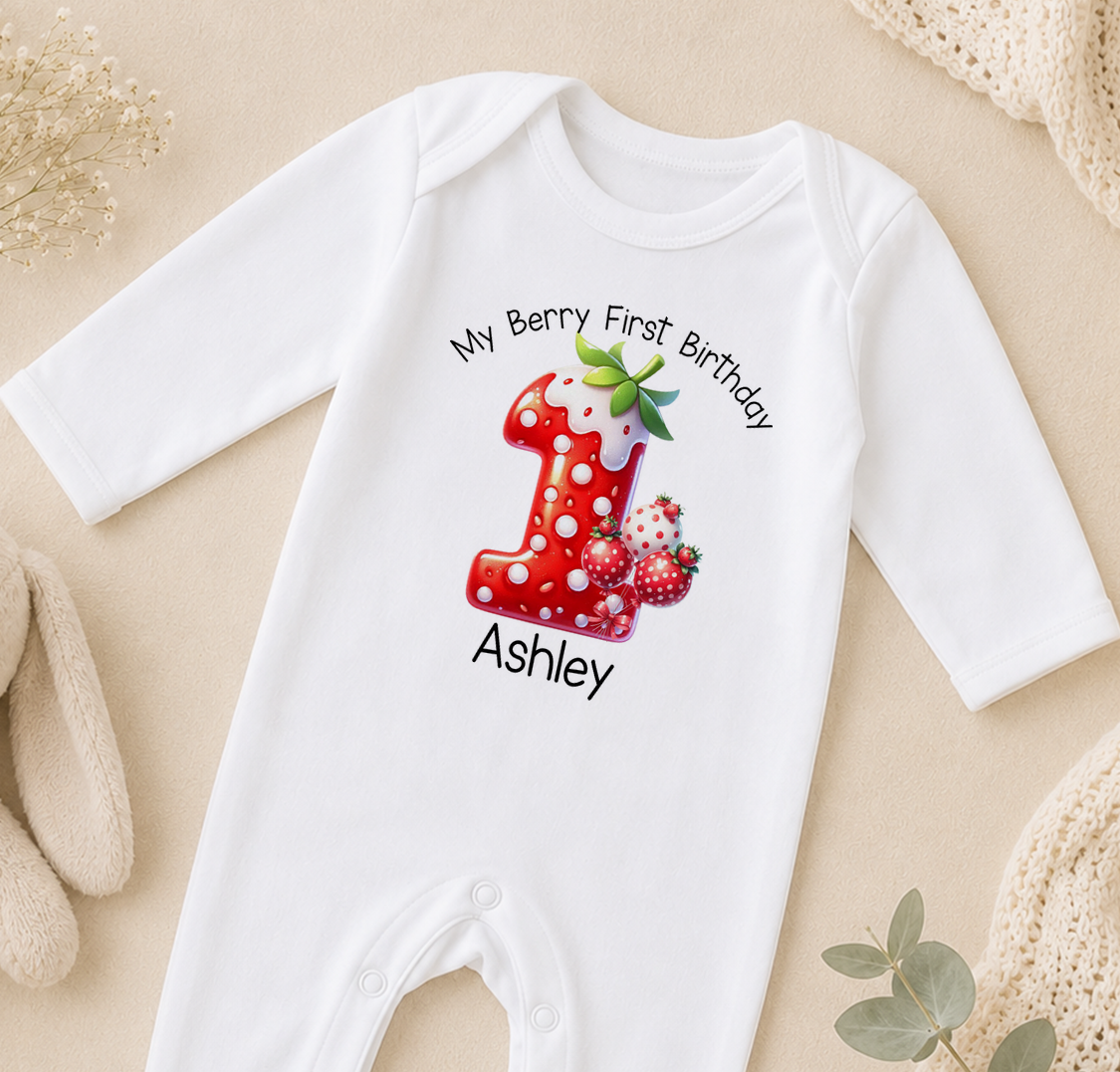 A white onesie with a red number one and strawberries printed on it, along with the text "My Berry First Birthday Ashley".