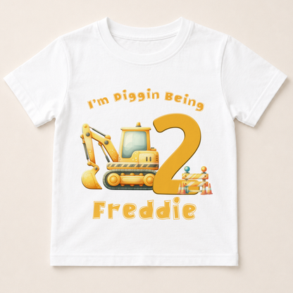 A white t-shirt with a cartoon construction vehicle and the text "I'm Piggin Being 2" printed on it.