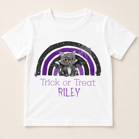 A white t-shirt with a graphic design featuring a cat and a rainbow. The cat is depicted as a bat-like creature, and the rainbow has purple and black colors. The text below the design says "Trick or Treat Riley".
