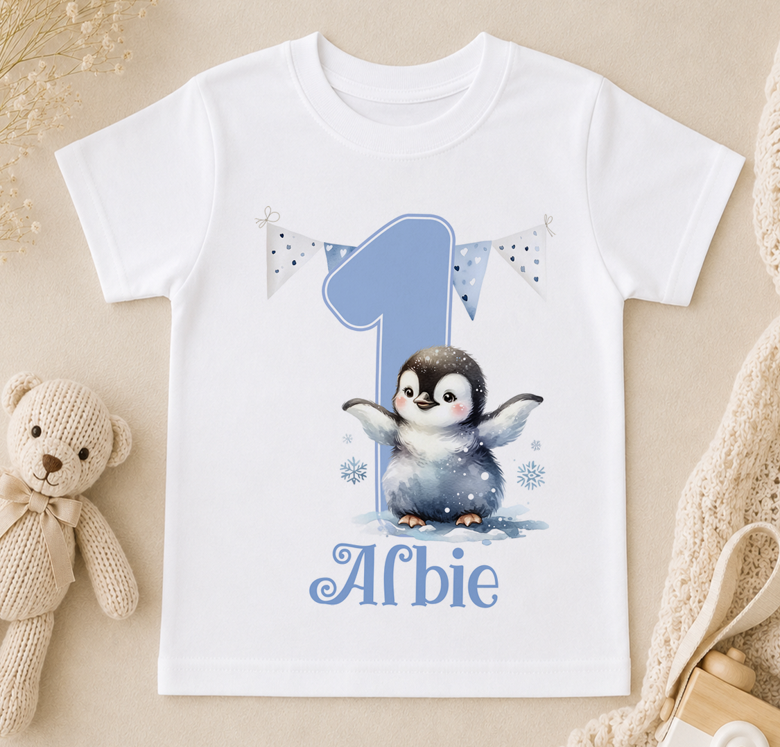 A white t-shirt with a penguin graphic and the number 1, along with the text "Alfie" printed on it.