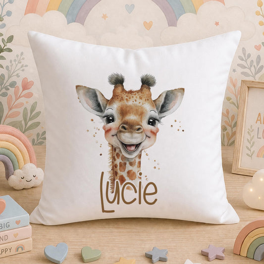 White square nursery cushion printed with an illustrated giraffe and the personalised name Lucie, photographed on a bed surrounded by soft toys and nursery decorations
