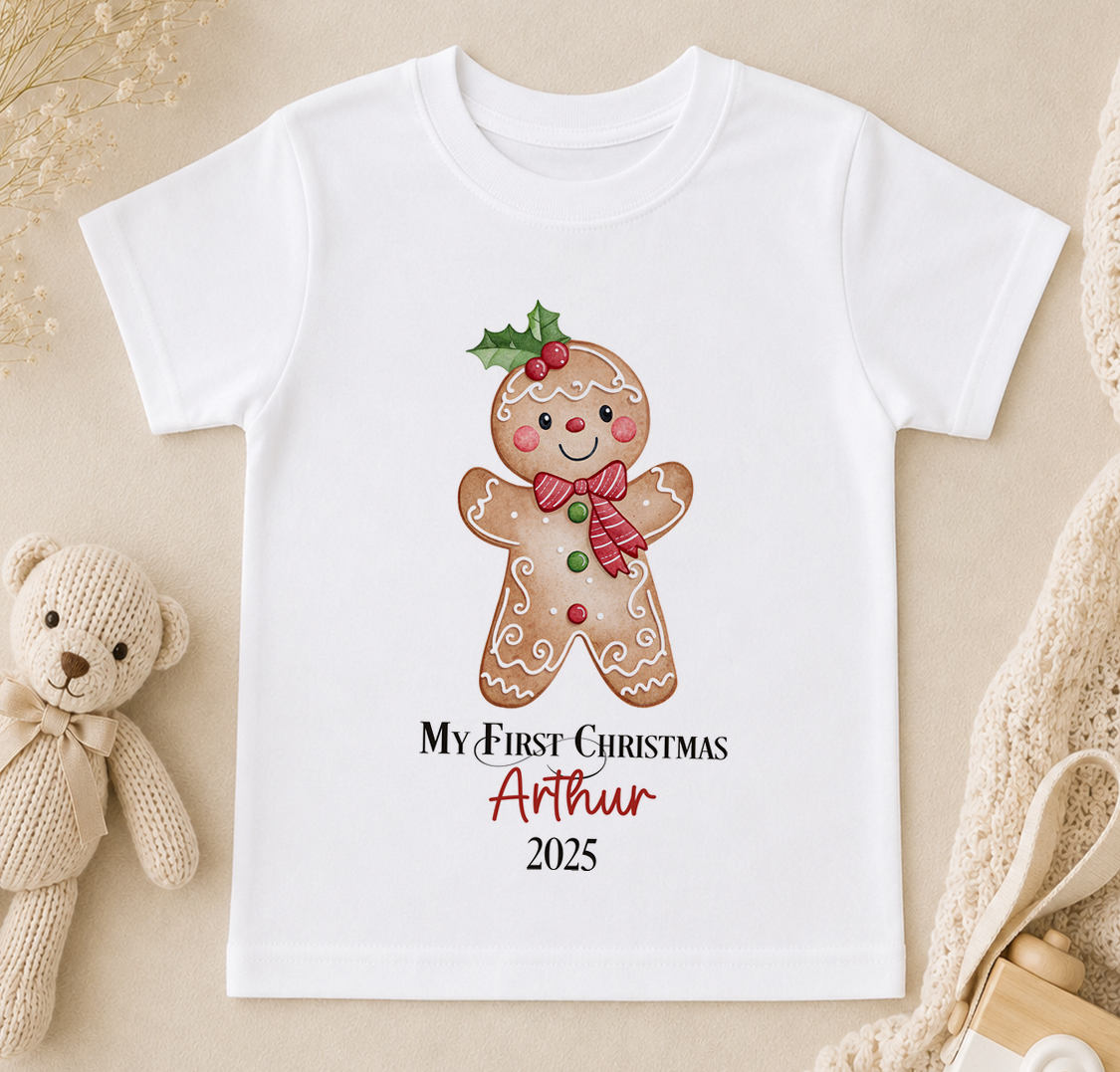 A white t-shirt with a gingerbread man graphic and text that says "My first Christmas Arthur 2020".