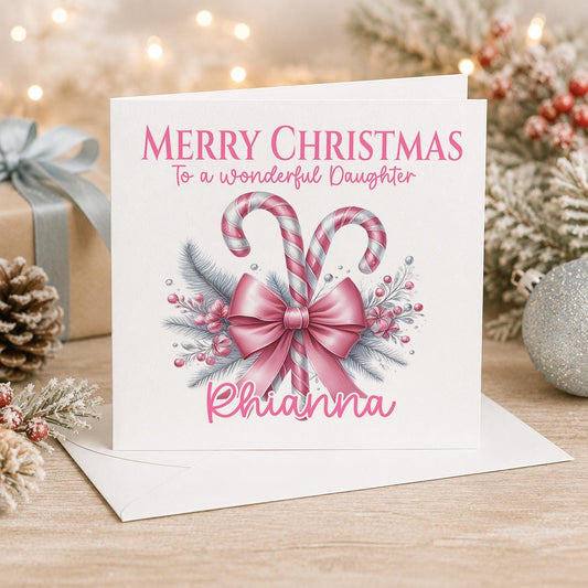 Personalised Christmas card, white 6x6 inch square card printed with a pink bow and candy canes, Merry Christmas and a name, standing beside a white envelope