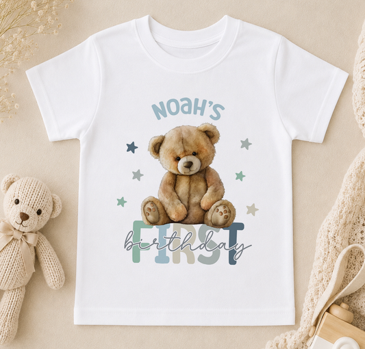 A white t-shirt with a teddy bear and the text "Noah's first birthday" printed on it, along with some stars.