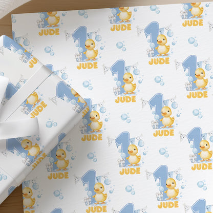 Flat lay of personalised blue duck first birthday wrapping paper with a name printed across the sheet
