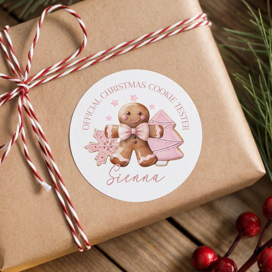 A brown gift box wrapped with red and white twine, featuring a round sticker with a gingerbread man and Christmas cookies.