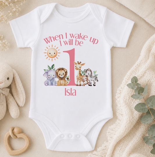 A white onesie with a printed design of various animals and the text "When I wake up I will be 1" printed on it, along with the name "Isla".
