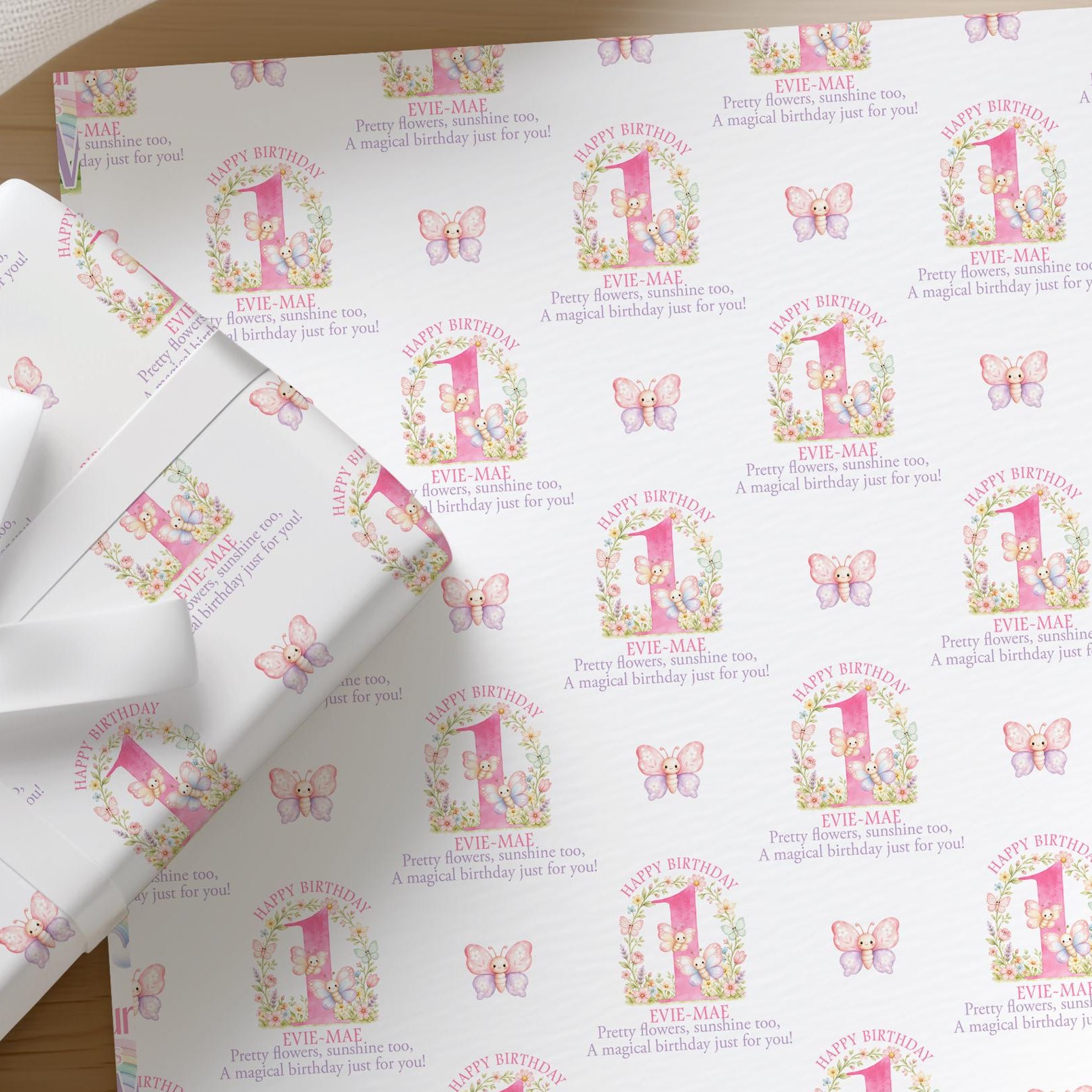 Flat lay of personalised floral pink butterfly wrapping paper for a girl's first birthday with a name printed across the sheet