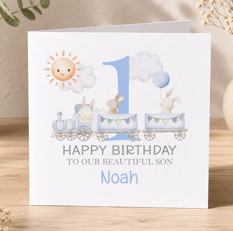 Personalised first birthday card featuring a blue train, bunnies, sun and clouds, printed with the example message Happy Birthday to our beautiful son Noah
