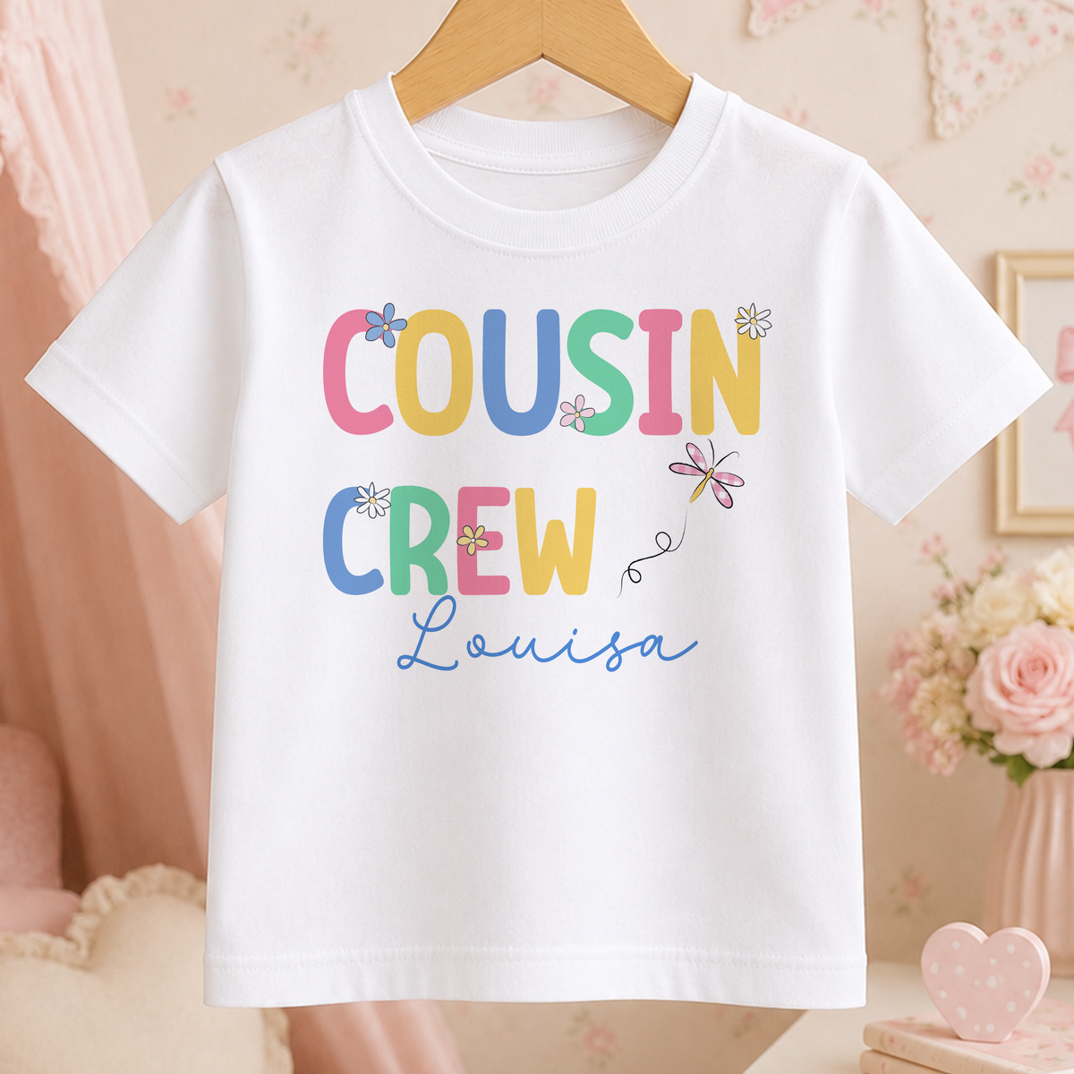 A white t-shirt with the text "COUSIN CREW Louisa" printed on it, along with colorful flowers and butterflies.
