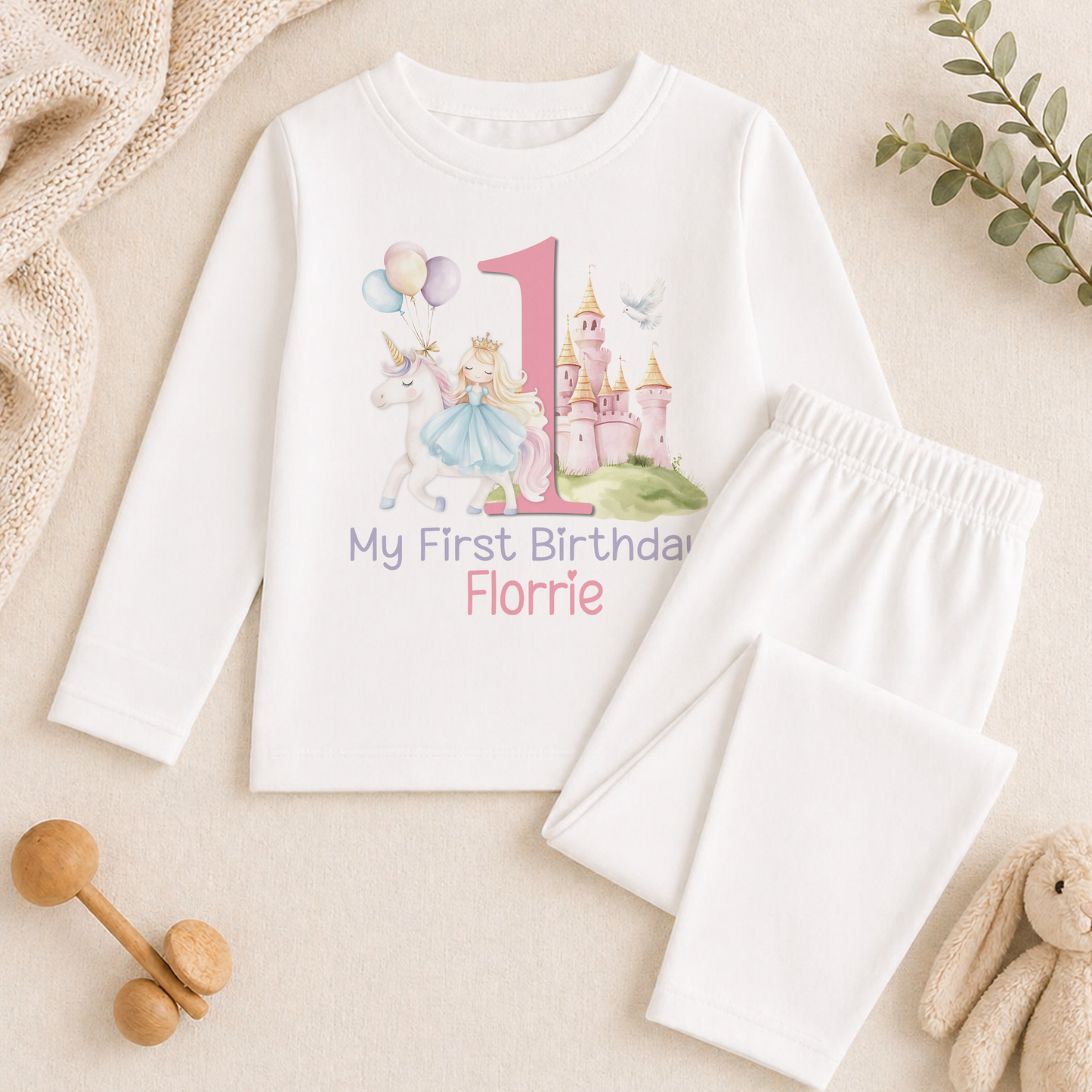 A white long-sleeved shirt with a princess and castle design, along with a pair of white pajama pants, and some stuffed animals.