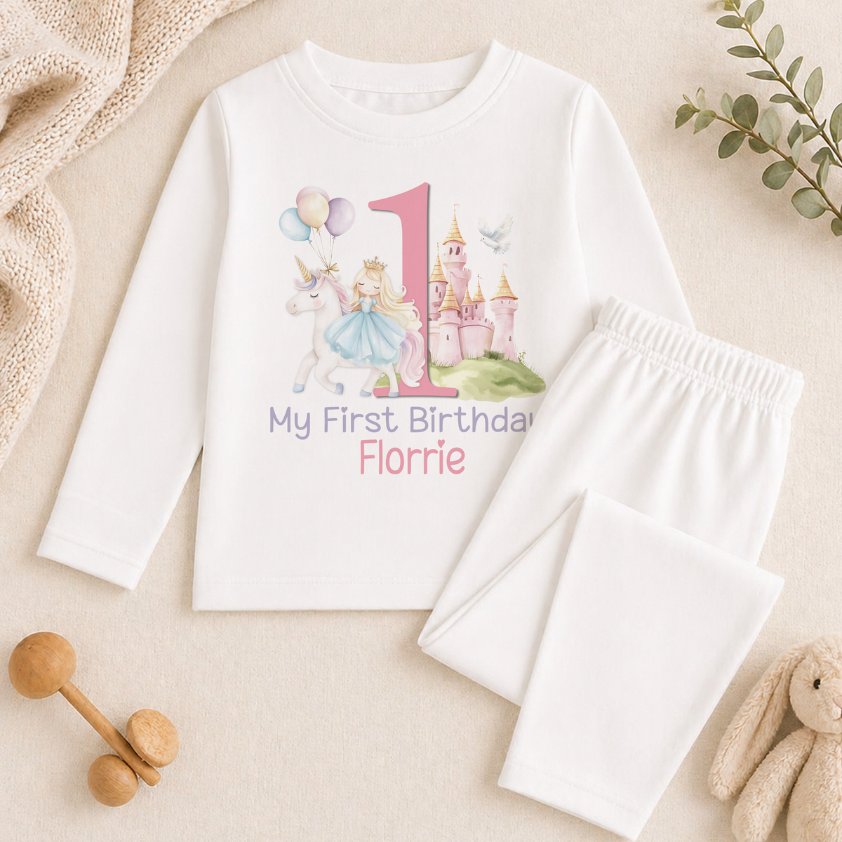 A white long-sleeved shirt with a princess and castle design, along with a pair of white pajama pants, and some stuffed animals.