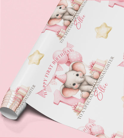 Roll of personalised first birthday wrapping paper featuring a repeating pink baby elephant, number one and balloon design.