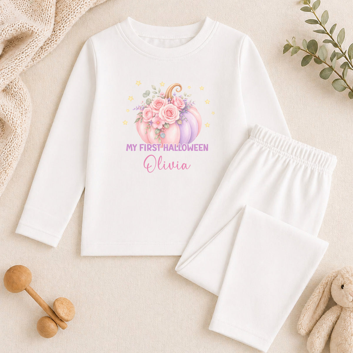 A white long-sleeved shirt with a pumpkin and floral design, along with white pajama bottoms, and a stuffed animal.