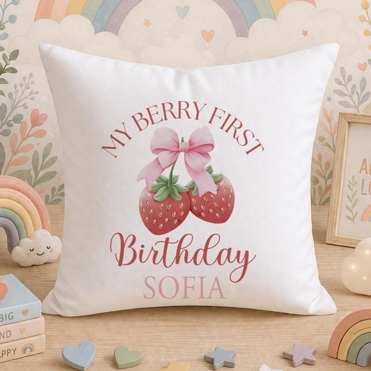 White plush cushion with a pink bow and strawberry design, personalised with the text 'My Berry First Birthday Sofia', styled with rainbow, cloud and teddy bear decorations.
