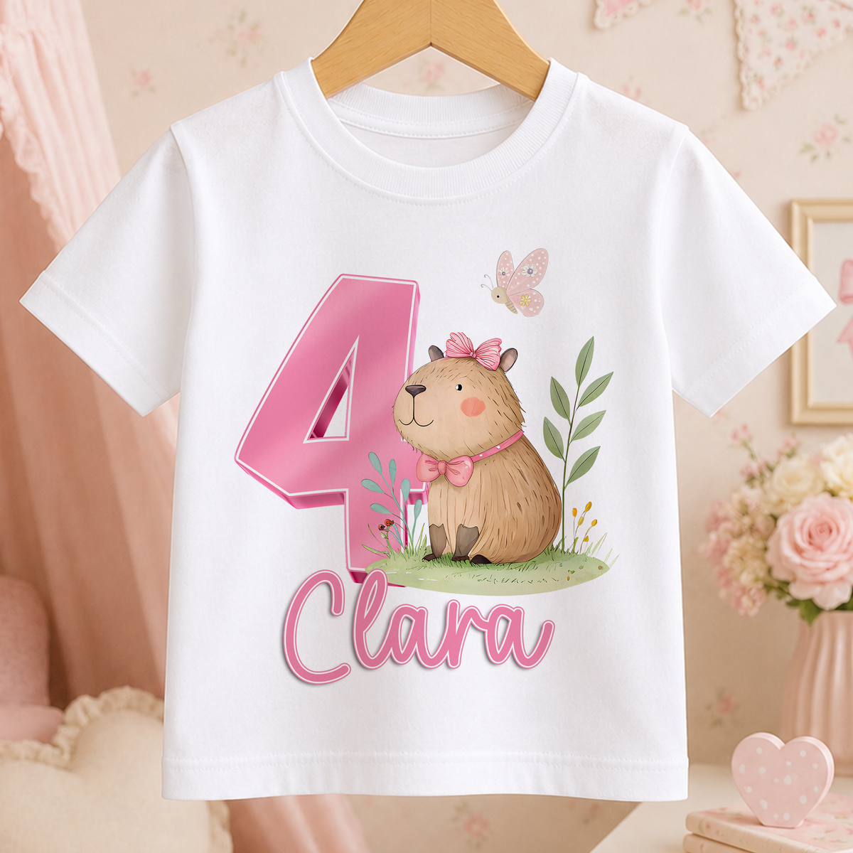 White t-shirt with a pink number 4 and a cartoon capybara wearing a bow tie, with the name "Clara" printed below