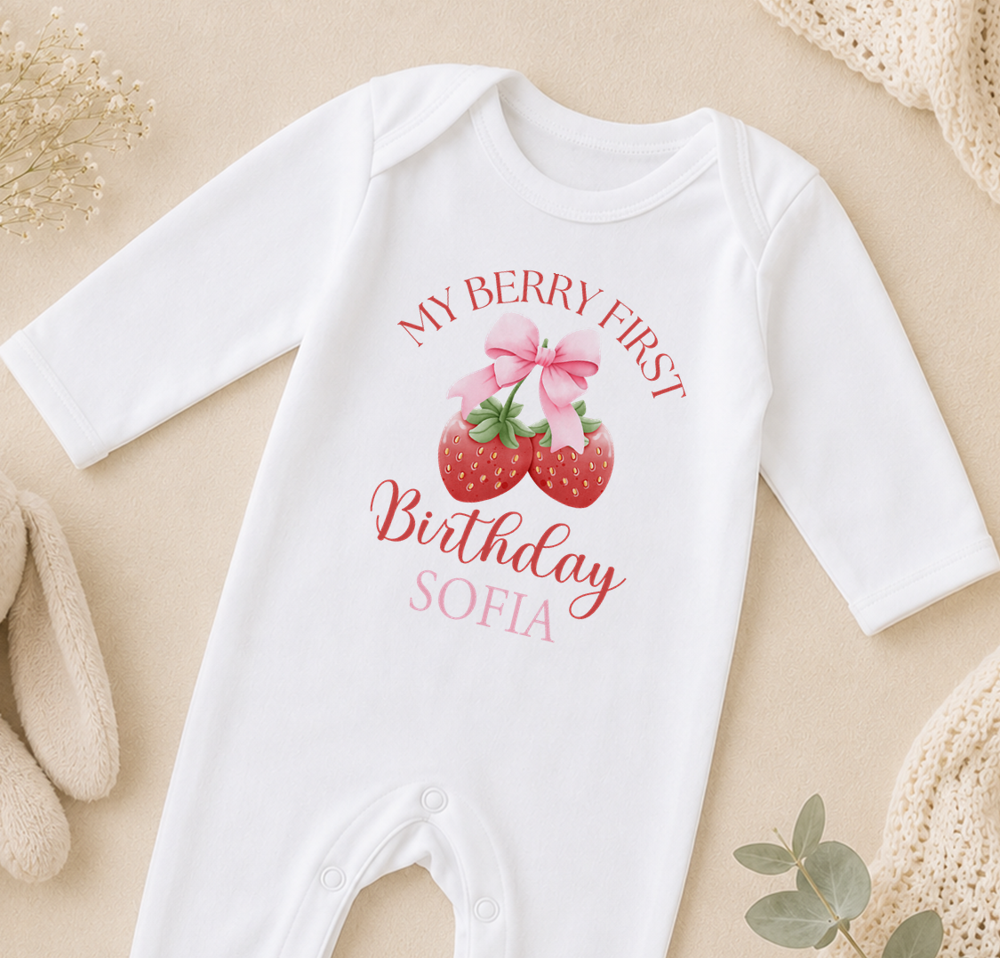 A white onesie with a personalized text and a strawberry graphic, likely for a baby's first birthday.