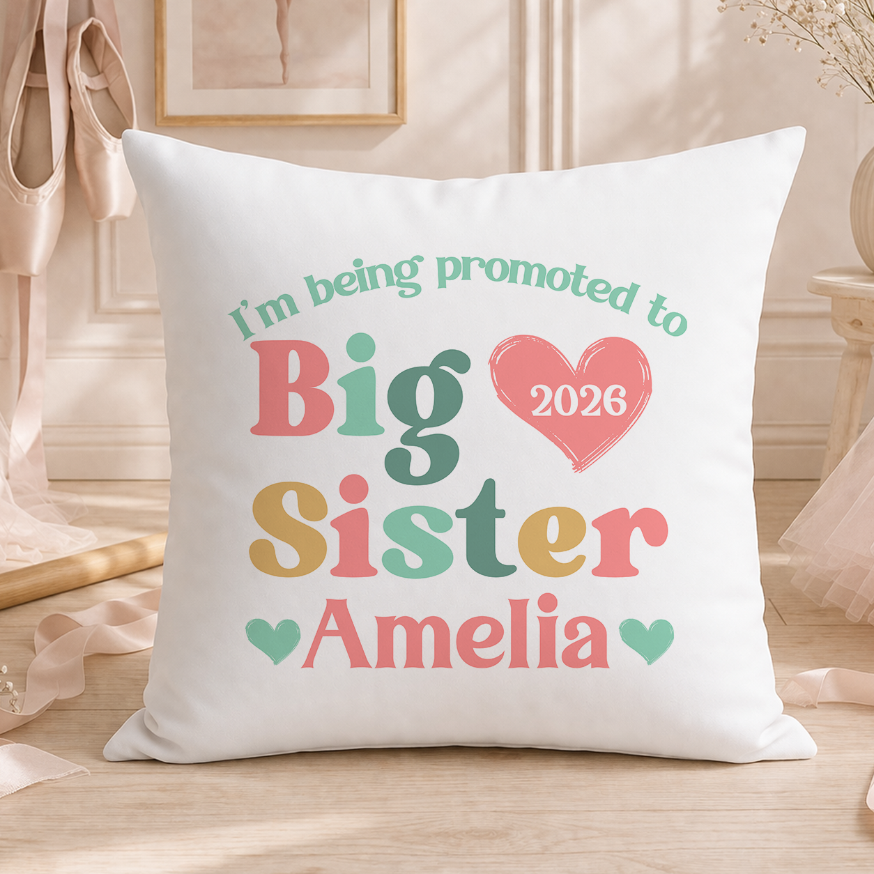 A white pillow with text that says "I'm being promoted to Big Sister Amelia" and a heart symbol.