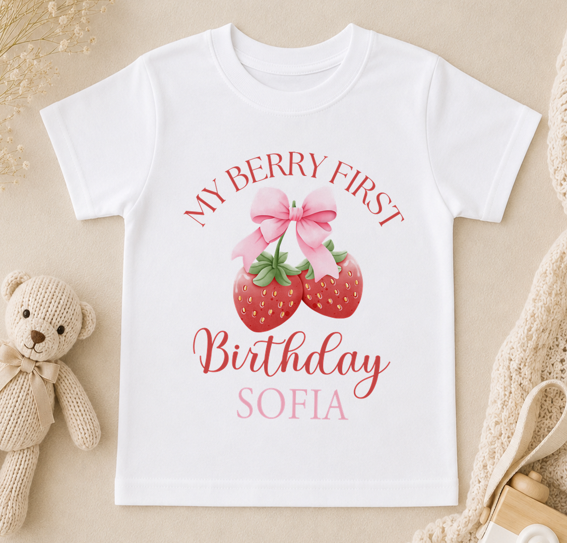 A white t-shirt with a graphic design featuring a strawberry and a pink bow, along with the text "My Berry First Birthday Sofia".