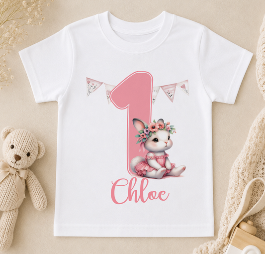 A white t-shirt with a pink bunny wearing a flower crown and the name "Chloé" written on it, along with a pink number one and pink banners.
