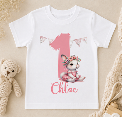 A white t-shirt with a pink bunny wearing a flower crown and the name "Chloé" written on it, along with a pink number one and pink banners.