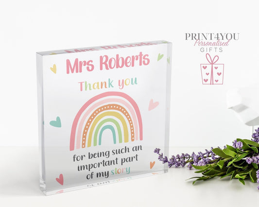 Clear freestanding acrylic block printed with 'Mrs Roberts, Thank you for being such an important part of my story' beside a pastel rainbow design, standing on a white desk.