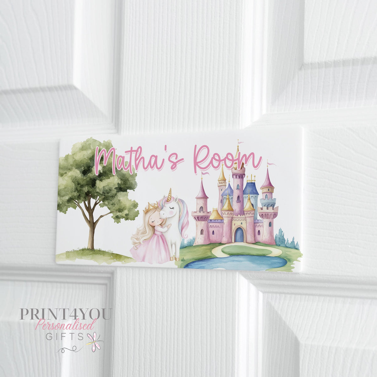 White acrylic door plaque on a panelled door, printed with a little girl hugging a unicorn beside a pink fairytale castle and a tree, with '[Name]'s Room' in pink script above the scene