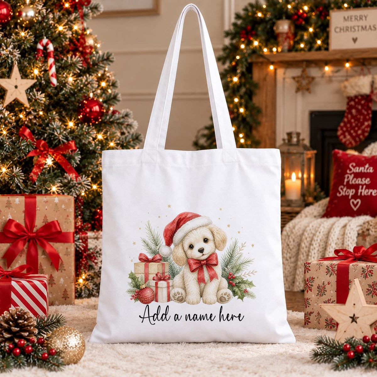 White cotton tote bag printed with a cream puppy in a red Santa hat sitting beside wrapped gifts, baubles and holly, above a name in script.
