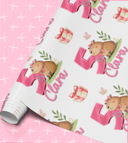 a pink background with a repeating pattern of a cartoon character, a gift box, and butterflies. The pattern includes the name "Clara" written in pink.