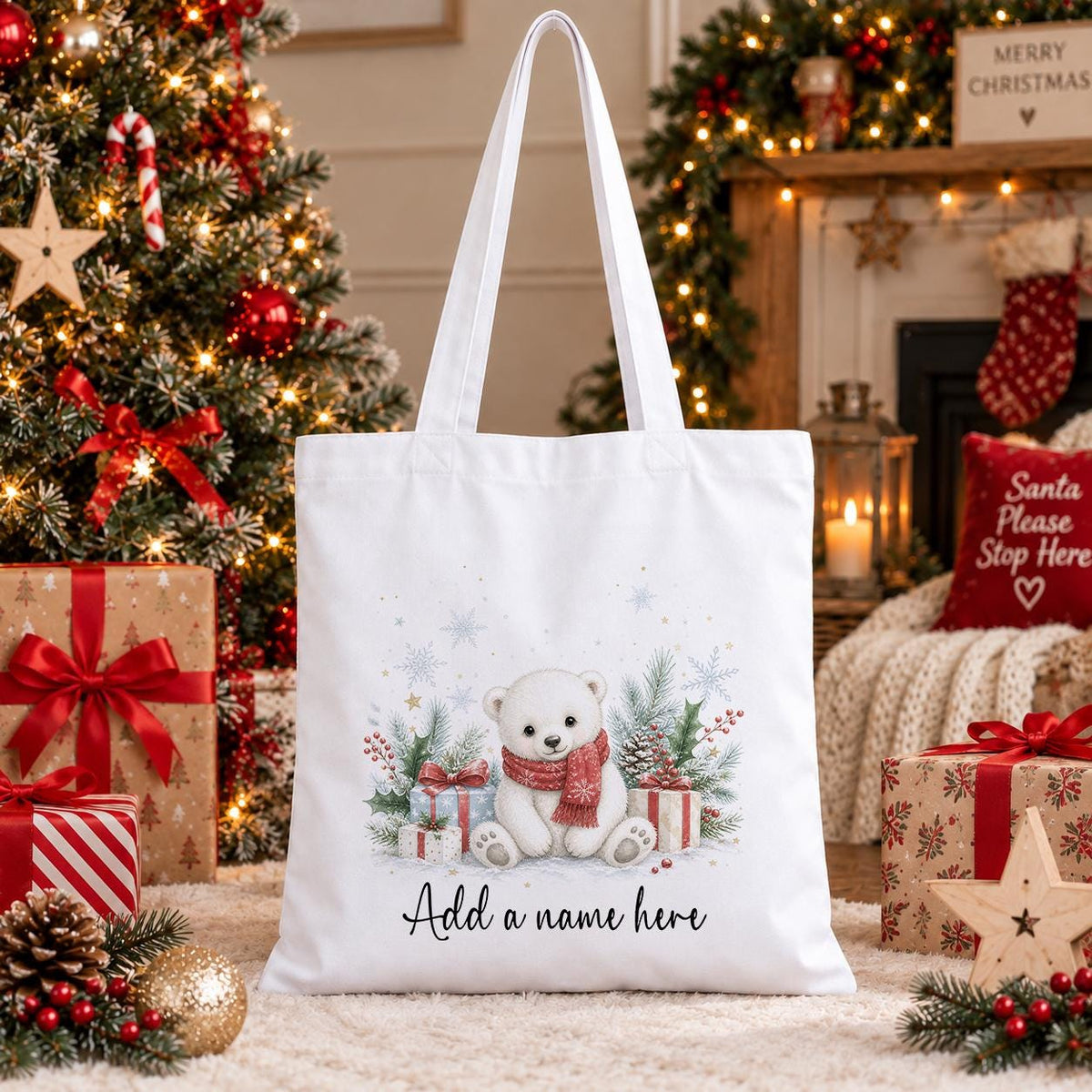 White cotton tote bag printed with a polar bear cub in a red scarf beside wrapped gifts, pine and snowflakes, above a name in script.