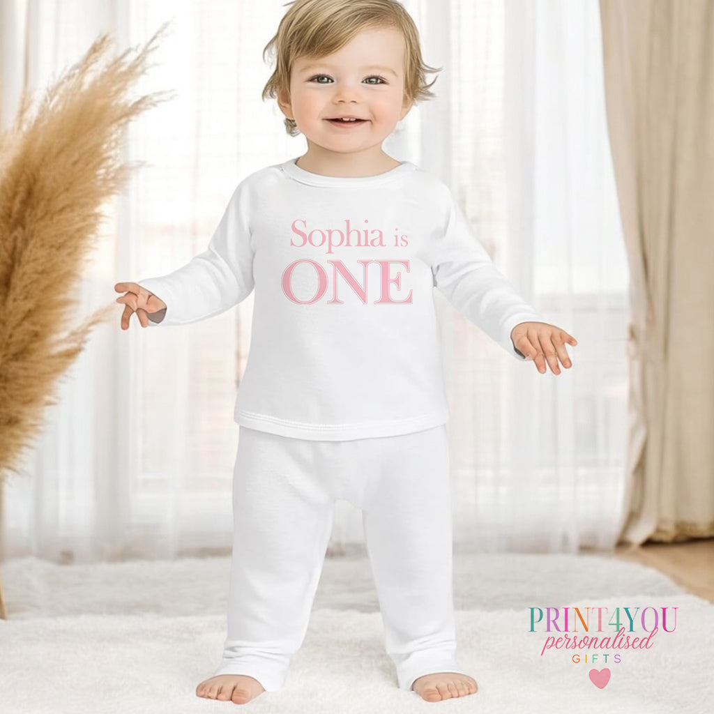 Personalised first birthday pyjamas in white cotton, printed with a pink number ONE and custom name, 1-2 years size.